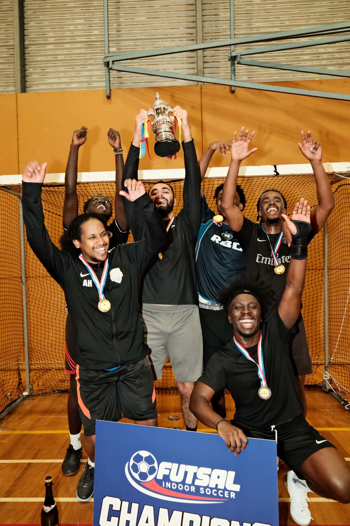 The team raises the trophy and celebrates with their medals in front of the goal.